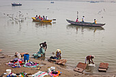 Arbeiter beim Wäschewaschen und im Hintergrund Pilger, die Möwen füttern, Fluss Ganges, Varanasi, Uttar Pradesh, Indien.