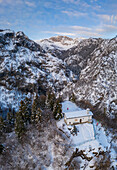 Luftaufnahme der kleinen Kirche San Peder und des Presolana-Passes während eines winterlichen Sonnenuntergangs. Rusio, Castione della Presolana, Val Seriana, Bezirk Bergamo, Lombardei, Italien.