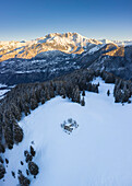 Luftaufnahme einer Berghütte und des Presolana-Massivs während eines Wintersonnenaufgangs vom Monte Pora, Val Seriana, Bezirk Bergamo, Lombardei, Italien.
