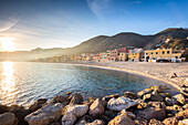 Nebliger Sonnenuntergang über den bunten Häusern und dem Strand von Varigotti, Finale Ligure, Bezirk Savona, Ponente Riviera, Ligurien, Italien.