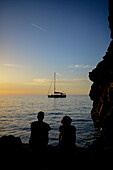 Couple of friends enjoying a sunset in Torrent de Pareis with sailing boat, Mallorca, Spain