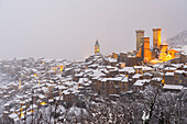 Das winterliche Panorama des beleuchteten mittelalterlichen Dorfes Pacentro mit dem Schloss, dem Glockenturm und dem schneebedeckten Haus, Gemeinde Pacentro, Nationalpark Maiella, Provinz L'aquila, Italien