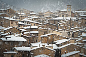 Old houses and the tower bell of the mountain village of Scanno under snowfall, Abruzzo national park, L’aquila province, Abruzzo, Italy