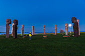 Mann mit gelber Jacke bewundert den hinter den Steinstatuen von Dodekalitten aufgehenden Vollmond in der Abenddämmerung, Insel Lolland, Seeland, Dänemark, Europa