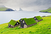 Traditionelle Häuser mit Grasdach mit Drangarnir und Tindholmur im Hintergrund, Bour, Insel Vagar, Färöer-Inseln, Dänemark, Europa