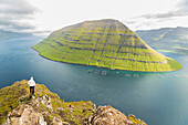 Wanderer steht auf einem Felsen der Klakkur-Spitze mit der Insel Kunoy im Hintergrund, Insel Bordoy, Färöer Inseln, Dänemark, Europa