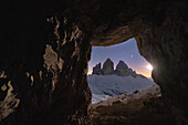 Tre Cime di Lavaredo lit by moon seen from opening in rocks of a war cave, Sesto Dolomites, Trentino-Alto Adige, Italy