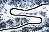 Aerial view of the s-shape mountain road along the winter forest covered with snow