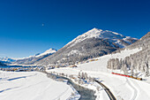 Clear sky on Bernina Express train in the snow on shore of Inn river, Madulain, Graubunden canton, Engadin, Switzerland