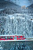 Bernina Express train crossing the snowy woods with Tarasp Castle on background, Graubunden canton, Lower Engadin, Switzerland