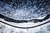 Snowplow on mountain road in the snowy woods on shore of frozen river, aerial view, Zernez, Engadin, Switzerland