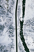 Leere Straße im Schnee, die den gefrorenen Wald und Fluss von oben durchquert, Engadin, Schweiz