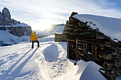 Rear view of man admiring sunset from traditional wood huts covered with snow, Passo Gardena, Dolomites, South Tyrol, Italy