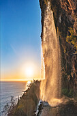 Gischt des mächtigen Anjos-Wasserfalls auf der Küstenstraße bei Sonnenuntergang, Ponta do Sol, Insel Madeira, Portugal