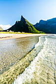 Waves crashing on sand beach with Hatten Mountain on background in summer, Ersfjord, Senja, Troms county, Norway