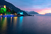 Colorful Christmas lights dressing the monument of Palazzo Gallio and buildings of Gravedona at dawn, Lake Como, Lombardy, Italy