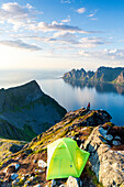 Hiker watching sunset out of camping tent on Husfjellet mountain peak, Senja island, Troms county, Norway