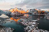 Winterlicher Sonnenaufgang über dem schneebedeckten Berg Olstind und der Bucht von Reine, Luftaufnahme, Reine, Nordland, Lofoten, Norwegen