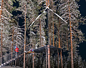 Hiker walking on steps leading to the cube shaped cottage with mirrors on the snowy trees, Tree hotel, Harads, Lapland, Sweden