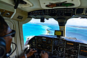 Pilot im Cockpit eines kleinen zweimotorigen Flugzeugs, der die idyllische Landschaft über dem türkisfarbenen Karibischen Meer bewundert