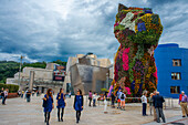 Jeff Koons' sculpture Puppy outside the Guggenheim Museum, Bilbao, Spain. Entrance of of Bilbao Guggenheim Museum reflected in Nervion River, Bilbao, Basque Country, Spain