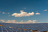 A field of solar panels at a solar power plant under a blue sky with puffy white clouds. Les Mees, Provence, France.