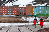 Men in arctic protective clothing walk past apartment buildings. Barentsburg, Spitsbergen Island, Svalbard, Norway.