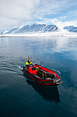 An inflatable raft cruises Mushamna Bay rimmed with mountains. Spitsbergen Island, Svalbard, Norway.