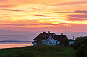 A fiery sunset sky reflects on the sea fronting an island home in Broennoysund. Broennoysund, Bronnoy, Nordland, Norway.