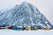 Bunte Häuser vor einem Berg im Winter. Noss, Vesteralen-Inseln, Nordland, Norwegen.