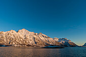 Schneebedeckte Küstenberge auf der Insel Stormolla, bei Sonnenuntergang. Stormolla-Insel, Lofoten-Inseln, Nordland, Norwegen.