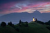 Kirche von Jamnik mit dem Berg Triglav im Hintergrund während des Sonnenaufgangs. Triglav-Nationalpark, Slowenien.