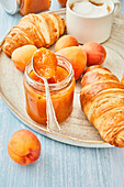Appetizing fresh croissant served with pot of homemade apricot jam on wooden cutting board