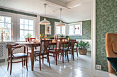 Dining room with wooden table, upholstered chairs and wallpaper with leaf motif