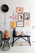 Black side table and wooden bench with vases and candle holders, pictures and wall light above bench