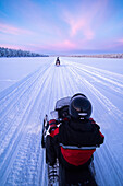 Snowmobiling on the frozen lake at sunset at Torassieppi, Lapland, Finland