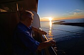 Älterer Mann, der die Zeit auf einem Kreuzfahrtschiff bei Sonnenuntergang im Mittelmeer überprüft