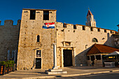 Südliches Stadttor von Trogir, Trogir, Dalmatinische Küste, Kroatien, Europa. Dieses Foto zeigt das südliche Stadttor von Trogir im goldenen Licht des frühen Morgens. Trogir ist eine wunderschöne alte Stadt an der dalmatinischen Küste Kroatiens, die dank ihrer atemberaubenden romanischen Kathedrale und Architektur auf der Liste des UNESCO-Weltkulturerbes steht. Die kopfsteingepflasterten Straßen der historischen Stadt Trogir sind übersät mit wunderschönen Gebäuden und hoch aufragenden Türmen, die es zu besichtigen und zu erkunden gilt. Nach der Besichtigung der St.-Lorenz-Kathedrale, des St.-L