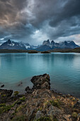 The rocky shoreline of Lago Pehoe in Torres del Paine National Park, a UNESCO World Biosphere Reserve in Chile in the Patagonia region of South America. Across the lake is the Paine Massif in the low clouds.