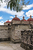 Stone fretwork panels in the ruins of the Zapotec city of Mitla. In the background are the domes of the Church of San Pablo. Mitla, Oaxaca, Mexico. A UNESCO World Heritage Site.