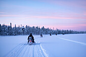 Schneemobilfahren auf dem zugefrorenen See bei Sonnenuntergang in Torassieppi, Lappland, Finnland