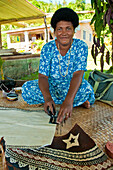Fidschianerin malt ein Muster auf Tapa-Stoff; Dorf Tongo, Insel Qamea, Fidschi.