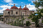 Kakteen und Laubsägearbeiten aus Stein in den Ruinen der zapotekischen Stadt Mitla. Im Hintergrund ist die Kirche von San Pablo zu sehen. Mitla, Oaxaca, Mexiko. Eine UNESCO-Weltkulturerbestätte.