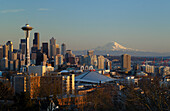 Skyline der Stadt bei Sonnenuntergang mit der Space Needle, dem Stadtzentrum und dem Mount Rainier vom Queen Anne Hill aus; Seattle, Washington.