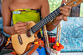 Beautiful local woman playing ukulele in Huahine island, Society Islands, French Polynesia, South Pacific. Coastline and lagoon of Huahine island near Maroe bay, south Pacific ocean, OceaniaSouth Pacific.