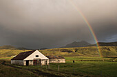 Typische isländische Bauernhöfe unter einem Regenbogen auf der Halbinsel Dyrholaey, in der Nähe von Vik, Südisland (Sudurland)