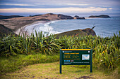 Schild des Te Paki Coastal Track, mit Te Werahi Beach dahinter, Cape Reinga, Neuseeland