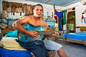 Innenansicht eines traditionellen Hauses in Rangiroa, Tuamotus-Inseln, Französisch-Polynesien, Südpazifik. Ein Mann spielt Gitarre und singt mit seiner Familie.