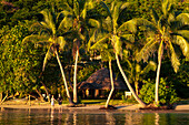 Couple on beach in front of bure guest room at Matangi Private Island Resort, Fiji.