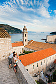 Touristen auf den Stadtmauern von Dubrovnik, Altstadt von Dubrovnik, Dalmatien, Kroatien. Dies ist ein Foto von Touristen auf den Stadtmauern von Dubrovnik. Es zeigt das Dominikanerkloster in der zum UNESCO-Weltkulturerbe gehörenden Altstadt von Dubrovnik. Für die meisten Touristen sind die Stadtmauern von Dubrovnik zweifellos der Höhepunkt eines Besuchs dieser schönen, historischen Altstadt an der dalmatinischen Küste Kroatiens. Die Stadtmauern von Dubrovnik bieten einen unvergleichlichen Panoramablick über die Altstadt von Dubrovnik und das Dominikanerkloster.